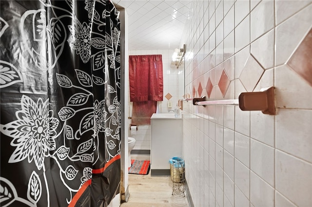 bathroom featuring tile walls, wood-type flooring, toilet, and sink