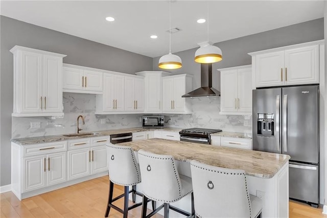 kitchen with stainless steel appliances, a kitchen island, a sink, white cabinetry, and wall chimney exhaust hood