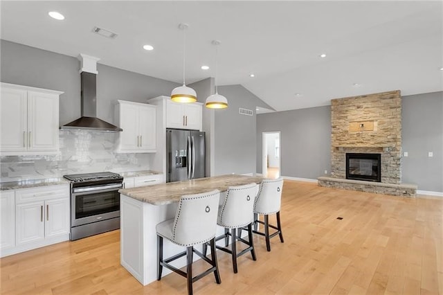 kitchen featuring stainless steel appliances, white cabinets, light wood-style flooring, and wall chimney exhaust hood