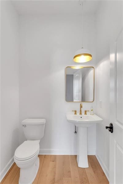 bathroom with toilet, baseboards, and wood finished floors