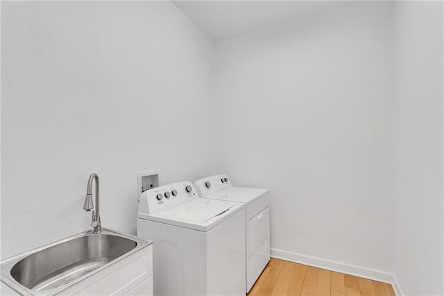 laundry room featuring light wood finished floors, cabinet space, a sink, independent washer and dryer, and baseboards