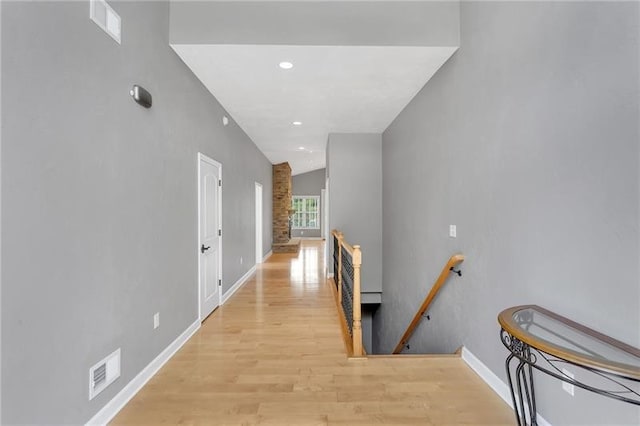 corridor with light wood-style floors, baseboards, visible vents, and an upstairs landing