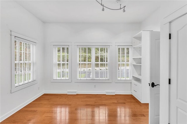 interior space featuring baseboards, light wood-style floors, visible vents, and a healthy amount of sunlight