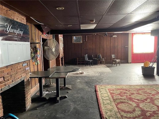 basement with wood walls, a fireplace, and a drop ceiling