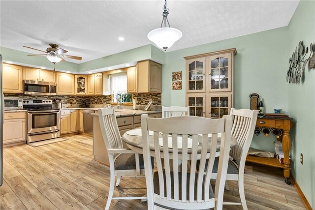 kitchen with appliances with stainless steel finishes, light hardwood / wood-style flooring, tasteful backsplash, hanging light fixtures, and light brown cabinetry