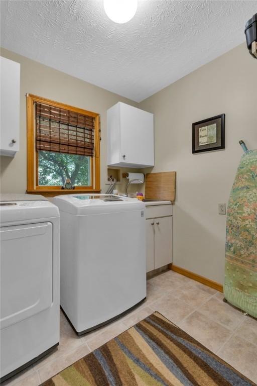 laundry room with washing machine and dryer, a textured ceiling, cabinets, and light tile patterned floors