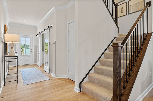 foyer entrance with light hardwood / wood-style flooring, a barn door, and ornamental molding