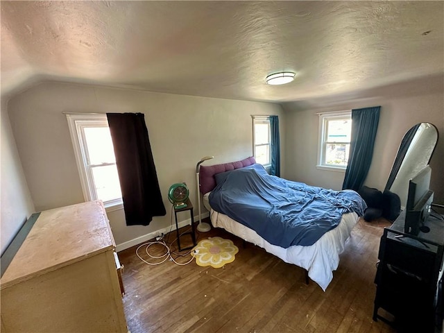 bedroom with dark wood-type flooring, lofted ceiling, multiple windows, and a textured ceiling