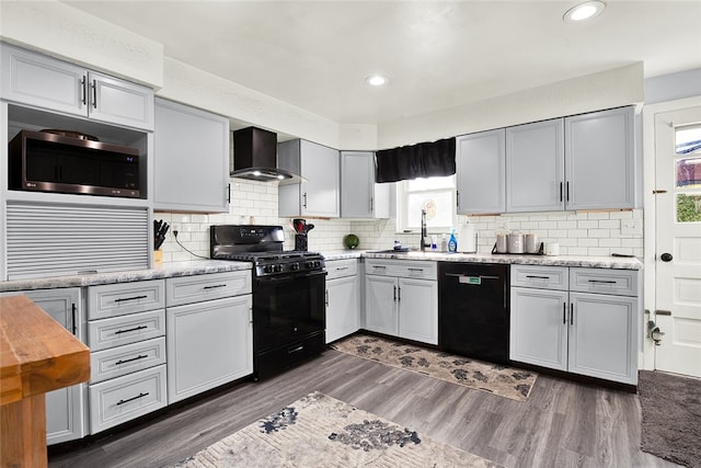 kitchen with wall chimney range hood, backsplash, dark hardwood / wood-style flooring, black appliances, and sink