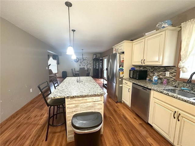 kitchen featuring stainless steel appliances, sink, pendant lighting, a kitchen island, and wood-type flooring