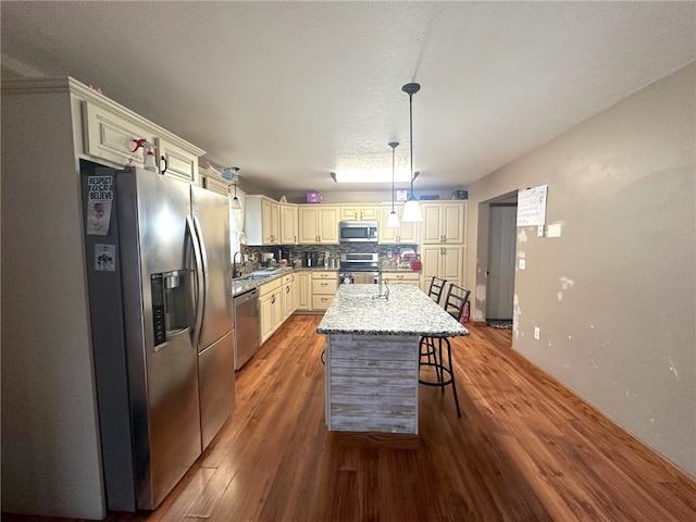 kitchen featuring backsplash, a center island, stainless steel appliances, hanging light fixtures, and hardwood / wood-style flooring