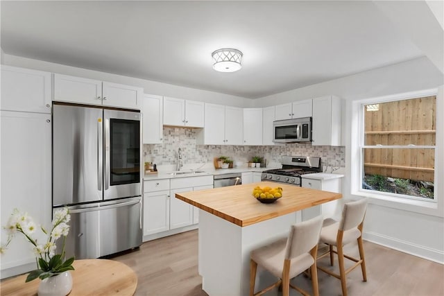 kitchen featuring stainless steel appliances, butcher block countertops, a breakfast bar, a sink, and tasteful backsplash