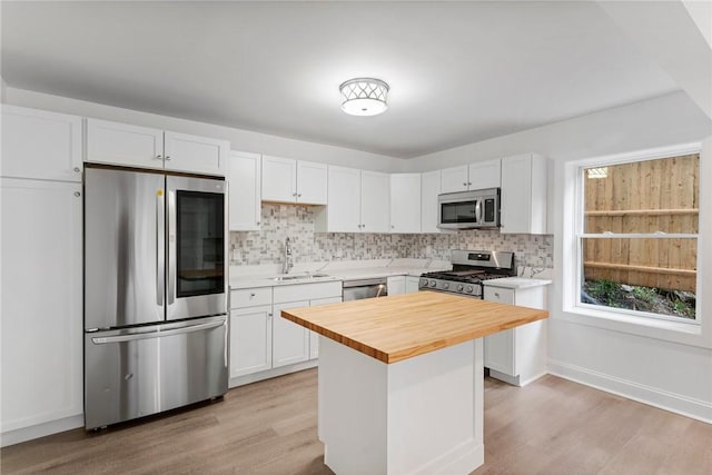 kitchen featuring stainless steel appliances, butcher block counters, a sink, white cabinets, and decorative backsplash