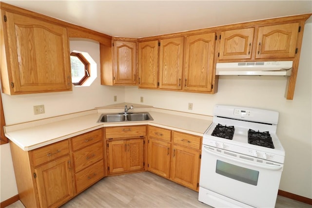 kitchen featuring brown cabinetry, gas range gas stove, light countertops, under cabinet range hood, and a sink