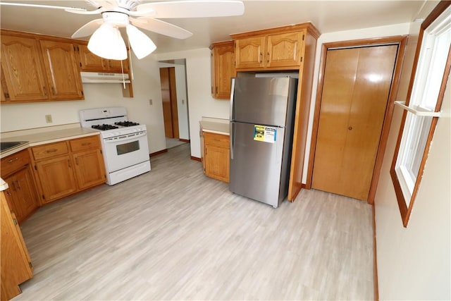 kitchen featuring freestanding refrigerator, light countertops, under cabinet range hood, and white gas range oven