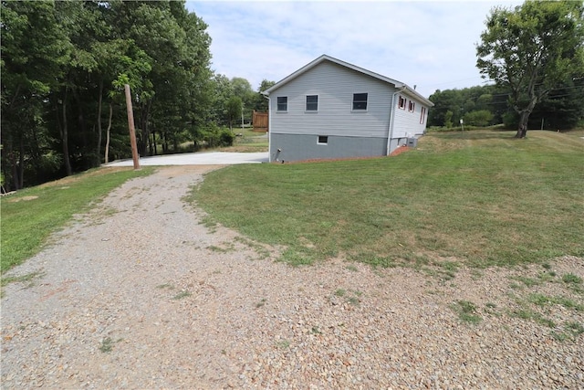 view of side of home with gravel driveway and a lawn