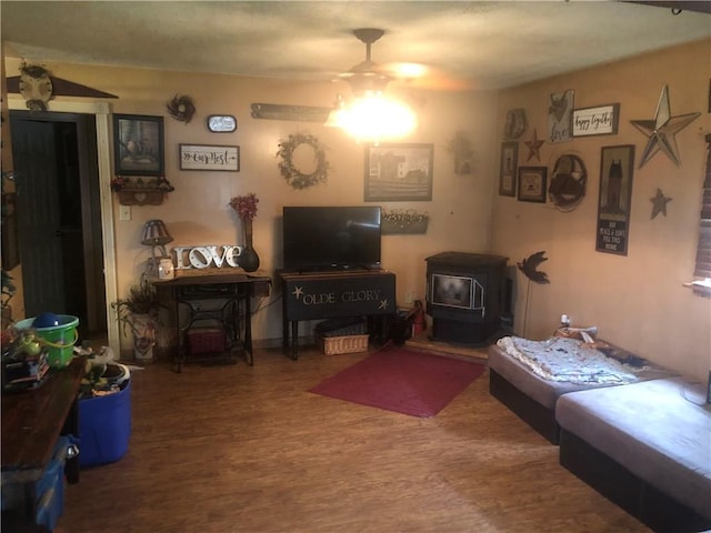 living room featuring wood-type flooring, a wood stove, and ceiling fan