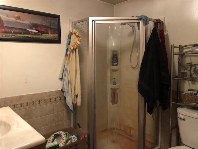 bathroom with vanity, toilet, a shower with shower door, and tile walls