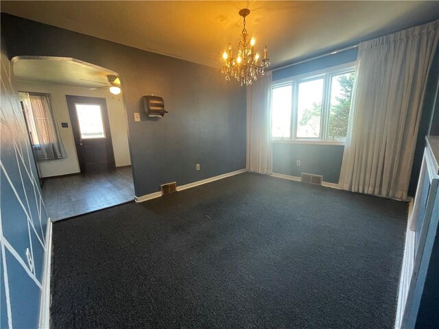 empty room featuring dark colored carpet and ceiling fan with notable chandelier