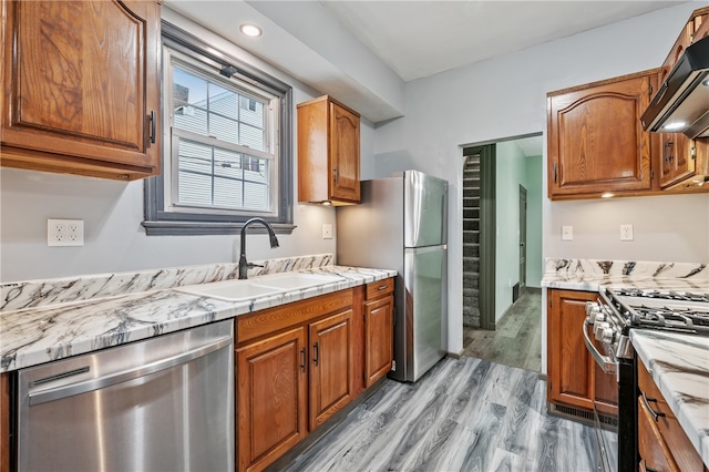 kitchen featuring light stone counters, stainless steel appliances, light hardwood / wood-style floors, custom exhaust hood, and sink