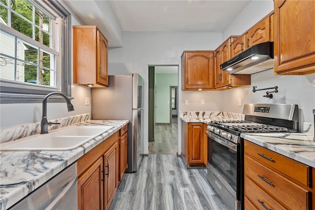 kitchen with light hardwood / wood-style floors, light stone countertops, appliances with stainless steel finishes, and sink