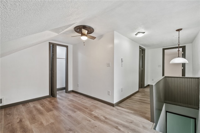 additional living space featuring light wood-type flooring, ceiling fan, vaulted ceiling, and a textured ceiling