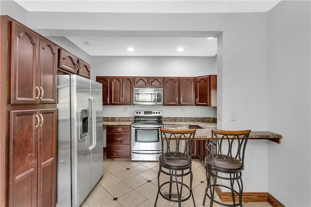 kitchen with kitchen peninsula, stainless steel appliances, light tile patterned floors, and a breakfast bar area