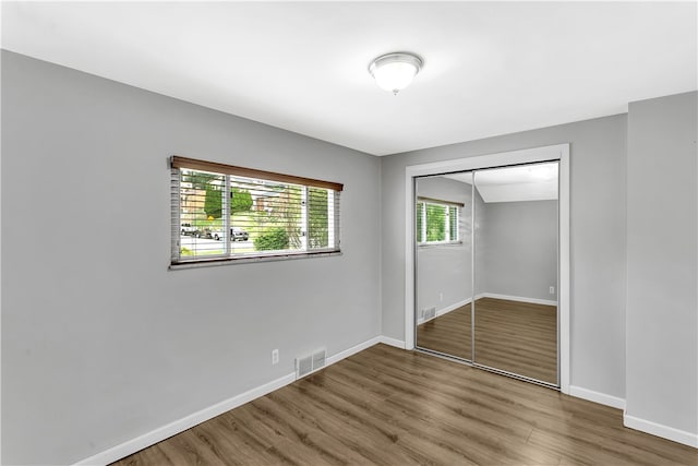 unfurnished bedroom with a closet, wood-type flooring, and multiple windows