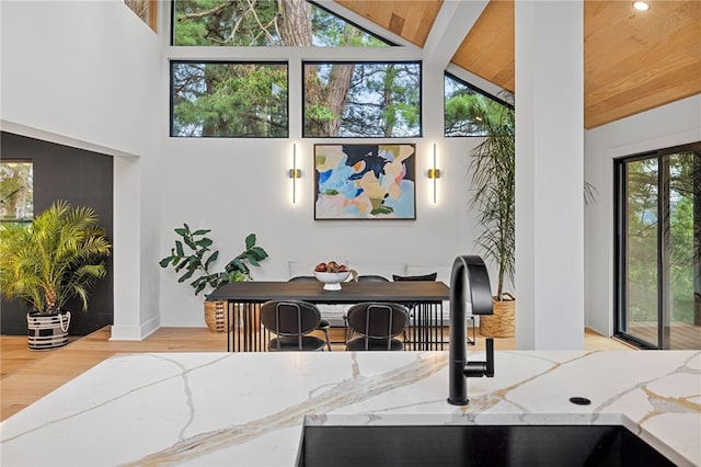 interior space featuring sink, wood ceiling, light hardwood / wood-style flooring, high vaulted ceiling, and light stone countertops