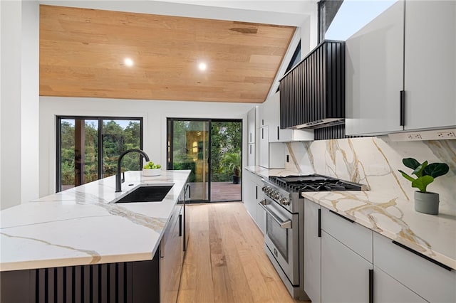 kitchen featuring sink, a kitchen island with sink, white cabinetry, stainless steel appliances, and light stone counters