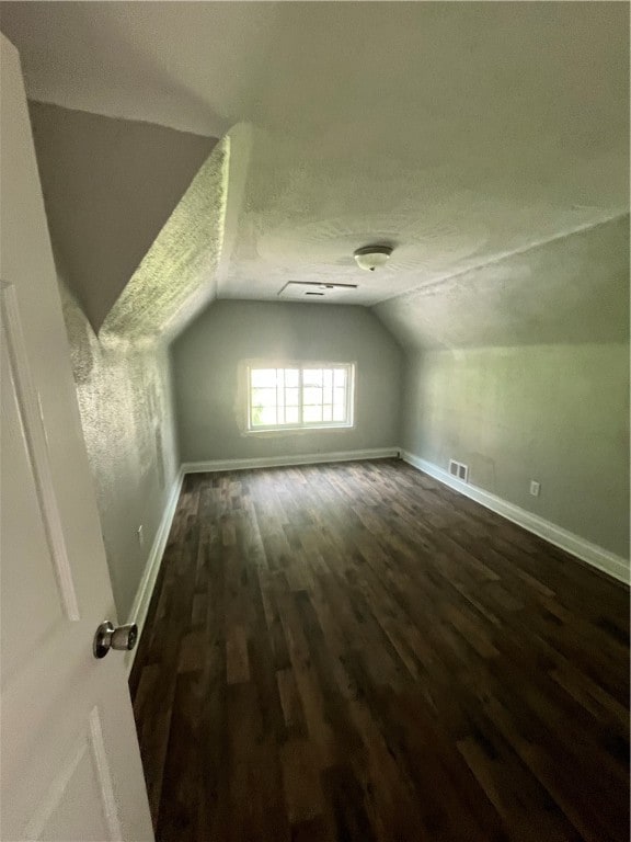 additional living space with a textured ceiling, dark hardwood / wood-style flooring, and lofted ceiling