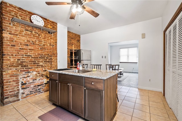 kitchen with brick wall, stainless steel refrigerator, light tile patterned floors, and ceiling fan