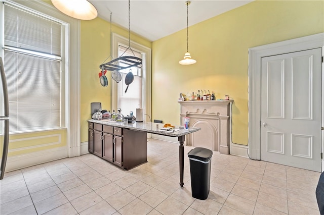 kitchen with dark brown cabinets, sink, hanging light fixtures, light tile patterned floors, and light stone countertops