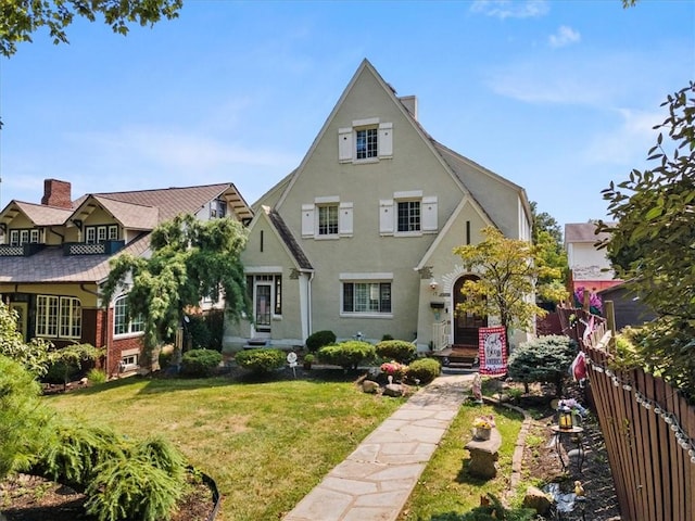 tudor-style house featuring entry steps, a front lawn, and fence