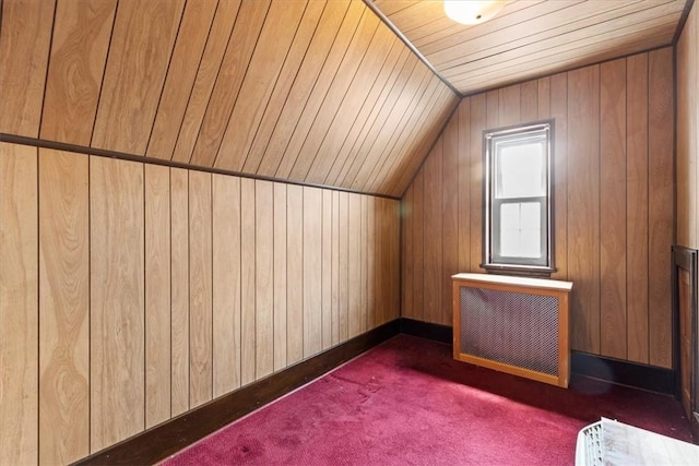 additional living space featuring vaulted ceiling, dark colored carpet, wood walls, and radiator