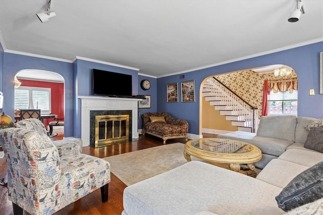 living area with arched walkways, dark wood finished floors, a premium fireplace, stairs, and crown molding