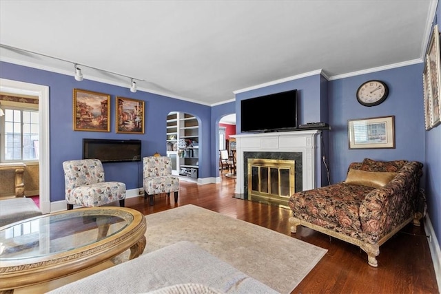 living room with built in shelves, a fireplace, crown molding, and wood finished floors