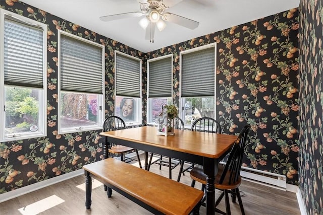 dining room with wallpapered walls, baseboards, wood finished floors, a baseboard heating unit, and a wealth of natural light