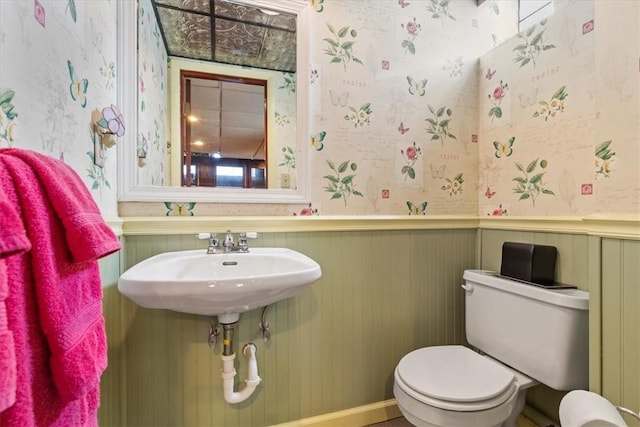 bathroom with toilet, wallpapered walls, and wainscoting