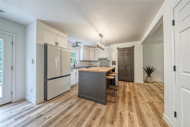 kitchen with butcher block countertops, refrigerator, white cabinets, decorative light fixtures, and a barn door