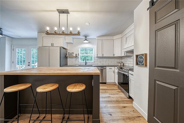 kitchen with appliances with stainless steel finishes, white cabinetry, tasteful backsplash, wood counters, and decorative light fixtures