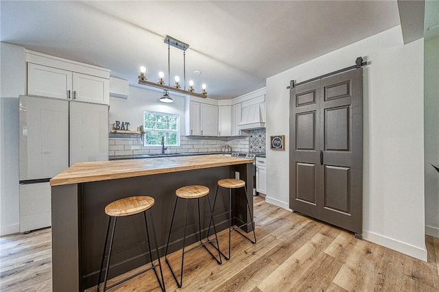 kitchen featuring wooden counters, decorative light fixtures, fridge, white cabinets, and backsplash