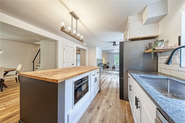 kitchen with butcher block countertops, decorative light fixtures, white cabinetry, sink, and light wood-type flooring