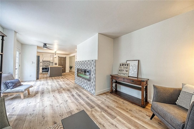 living room featuring ceiling fan, a tiled fireplace, and light hardwood / wood-style floors