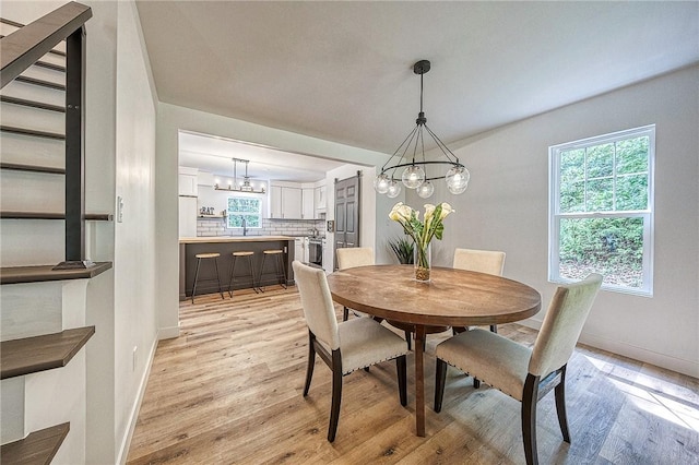 dining space with sink, a notable chandelier, and light wood-type flooring