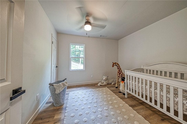 bedroom with a crib, hardwood / wood-style floors, and ceiling fan