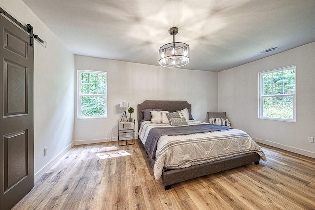 bedroom with multiple windows, a notable chandelier, light hardwood / wood-style floors, and a barn door