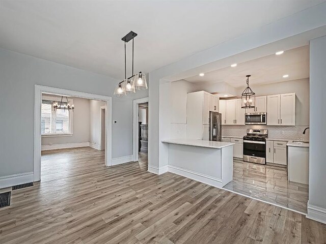 kitchen with light tile patterned floors, kitchen peninsula, white cabinets, appliances with stainless steel finishes, and decorative light fixtures