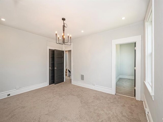 unfurnished bedroom featuring an inviting chandelier and light colored carpet