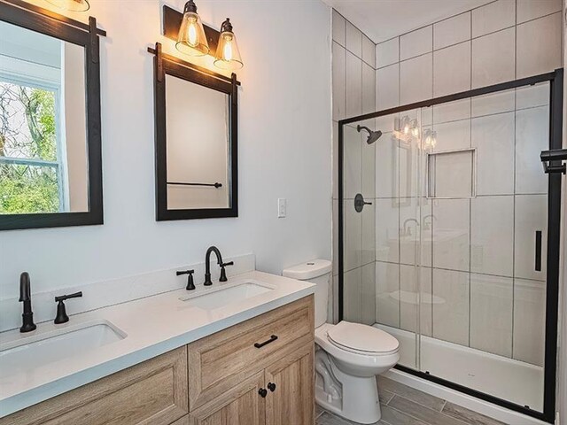 bathroom featuring a shower with shower door, dual bowl vanity, and toilet